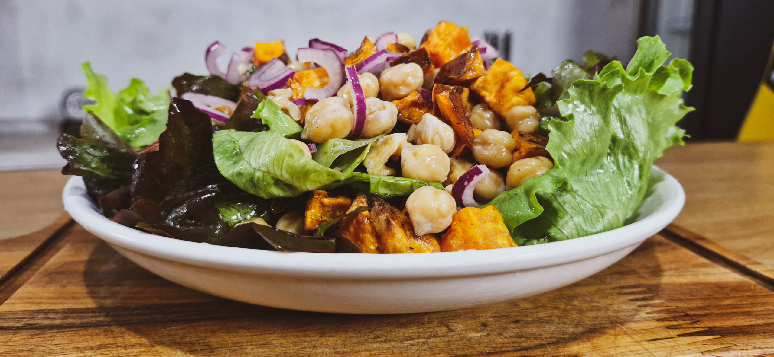 Salada de Batata Doce com Grão de Bico servida em uma tigela, com batatas douradas, grão de bico, cebola roxa, espinafre fresco e nozes, temperada com azeite e limão.