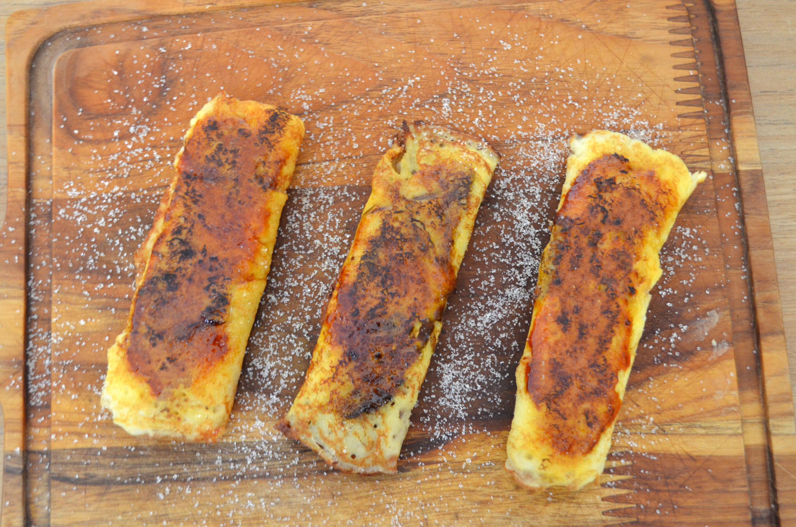 Panquecas douradas e recheadas com doce de leite, caramelizadas na superfície, servidas em um prato ao lado de frutas frescas e uma churrasqueira ao fundo.