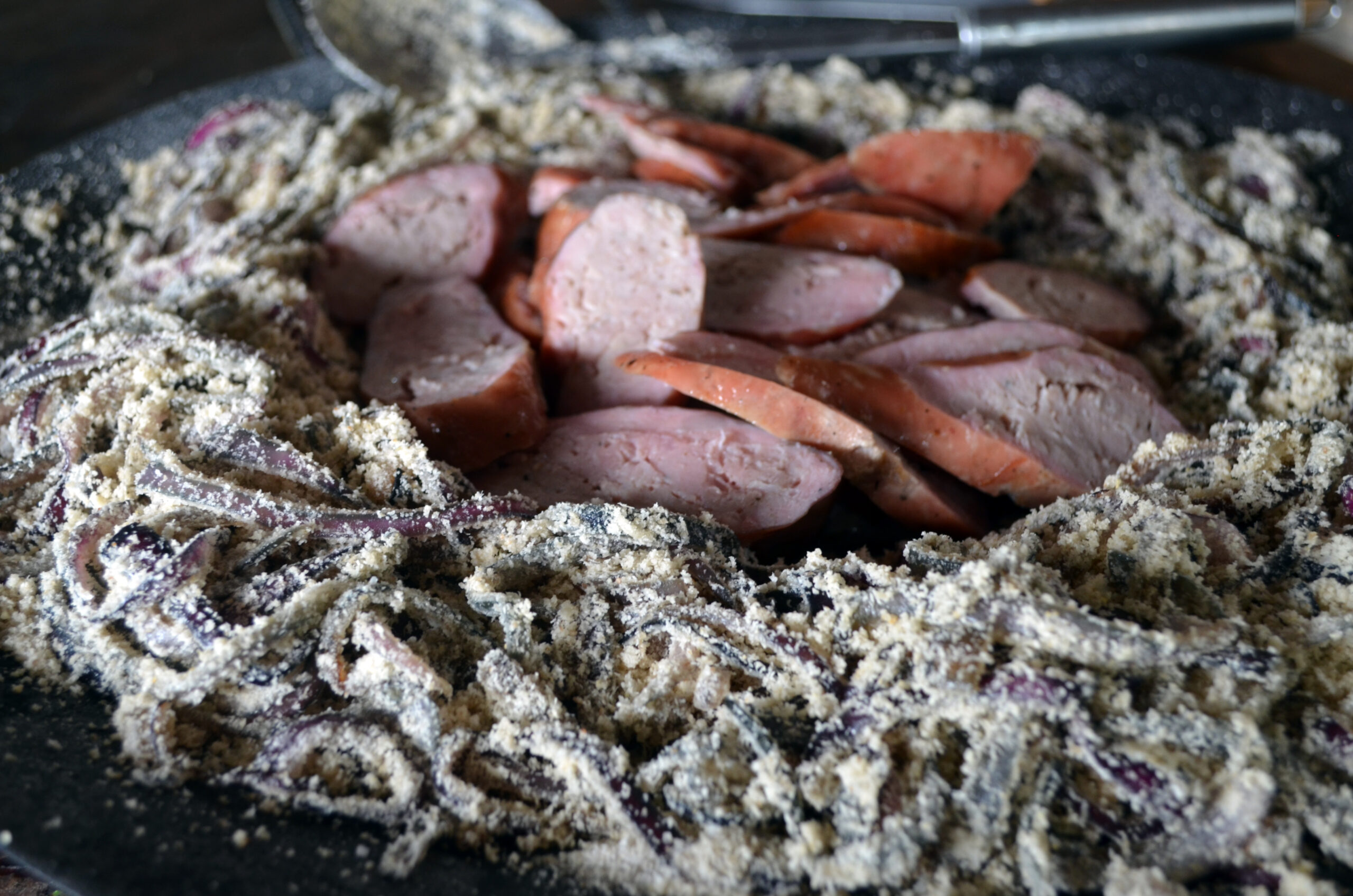 Prato com linguiça no varal, grelhada, acompanhada de farofa de cebola tostada em uma apresentação rústica.