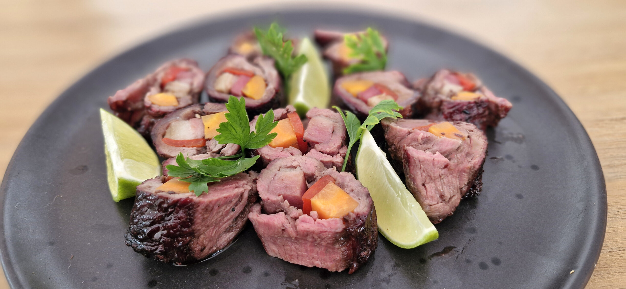 Espetinhos a Rolê prontos, com carne dourada, bacon crocante e recheio de vegetais coloridos, servidos em uma tábua ao lado de acompanhamentos.