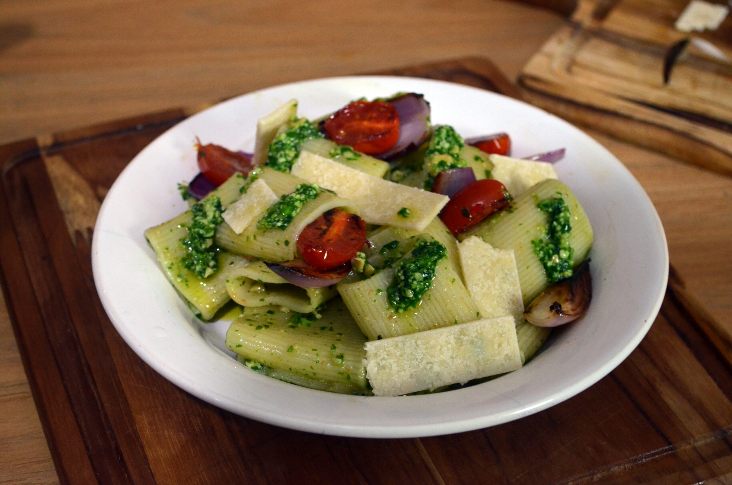 Prato de rigatoni ao pesto de rúcula com tomates caramelizados e lascas de parmesão.