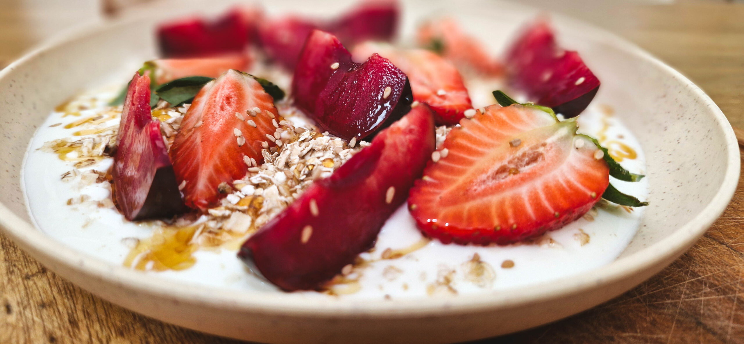 Bowl de iogurte grego com frutas vermelhas, chia e mel em uma tigela branca.