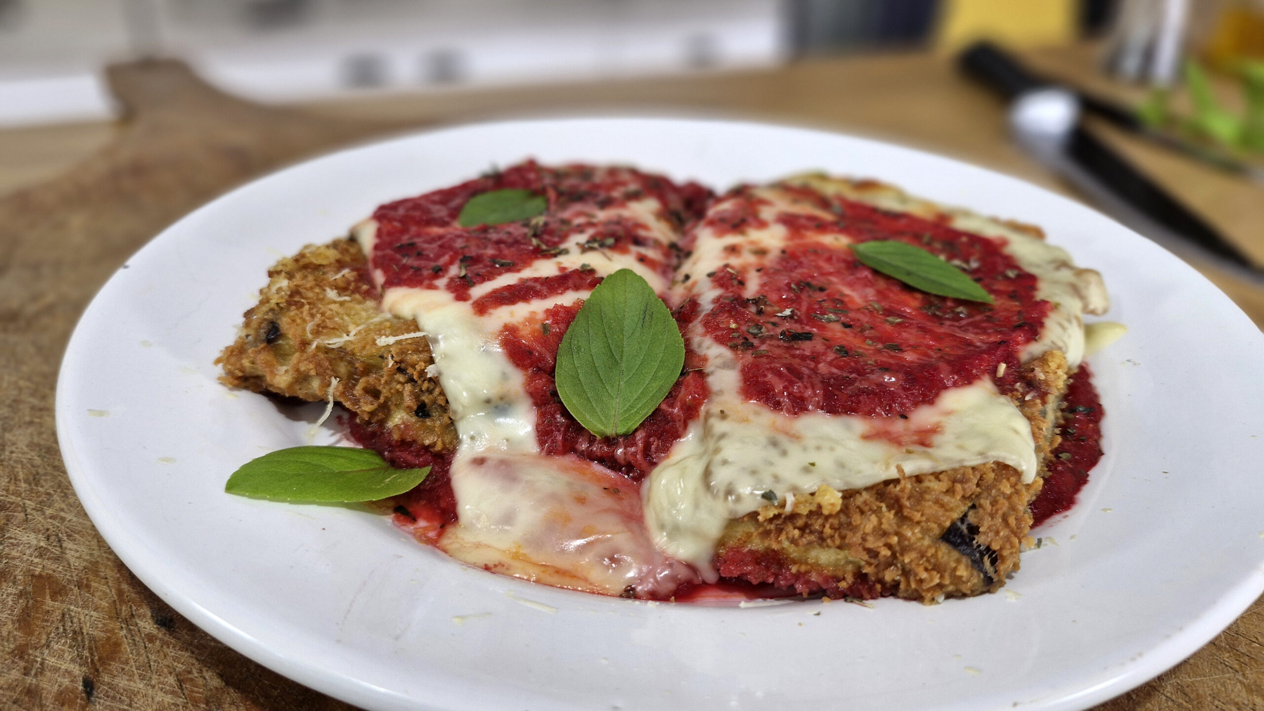Parmegiana de berinjela gratinada com queijo derretendo, servida em um prato rústico.