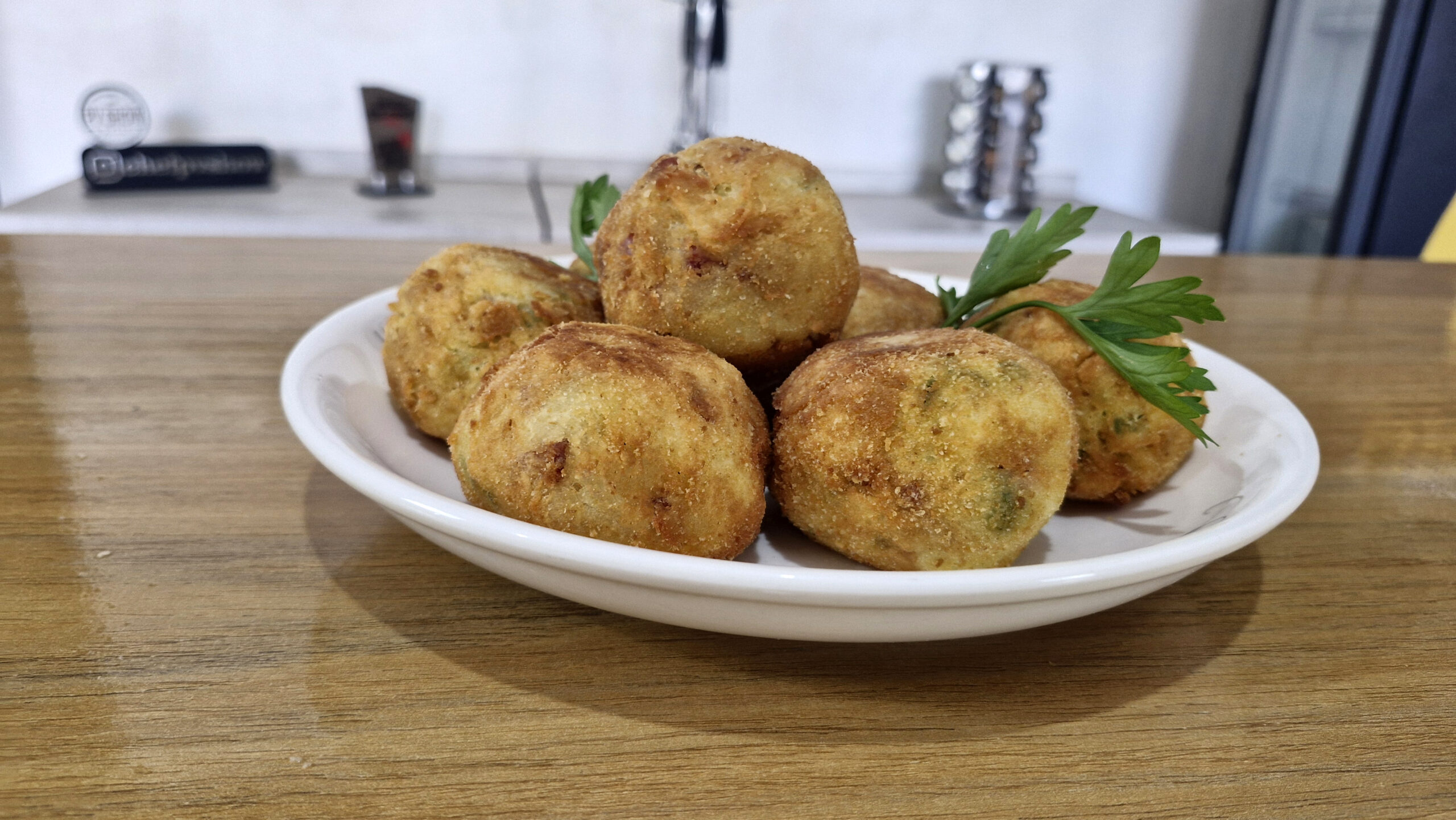 Bolinhos de purê de batata fritos, recheados com queijo cheddar derretendo, servidos douradinhos em uma tábua com molho de acompanhamento.