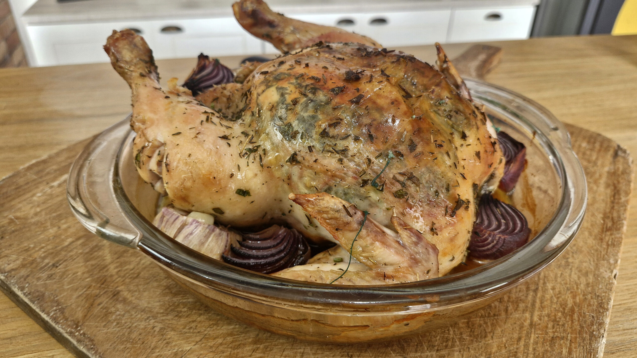 Frango assado inteiro, dourado, com pele crocante, servido com cebolas assadas e molho caseiro em uma travessa rústica.