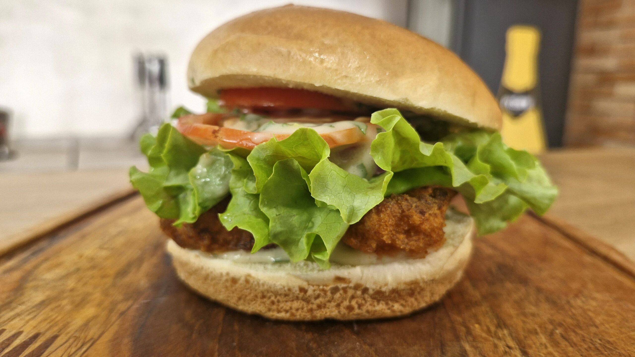 Sanduíche vegano com bife de couve-flor empanado, alface, tomate, cebola roxa e molho ranch em pão artesanal
