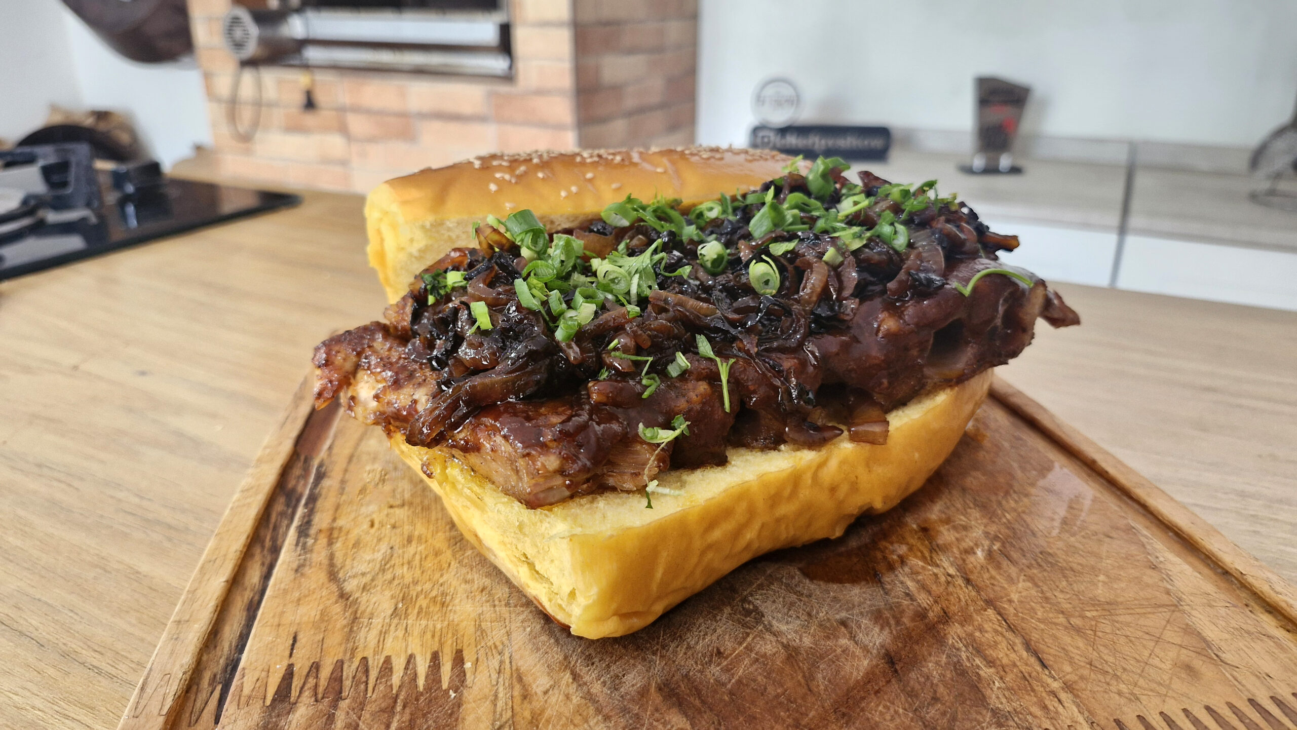 Sanduíche gigante de costela desossada com molho barbecue, servido no pão rústico com cebolas caramelizadas e picles, em uma tábua de madeira