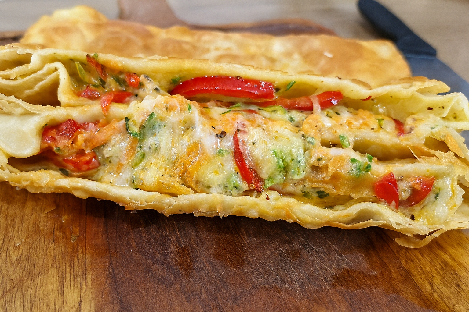 Pastel vegetariano dourado e crocante, recheado com legumes salteados e queijo derretido, servido em um prato rústico sobre bancada de madeira.
